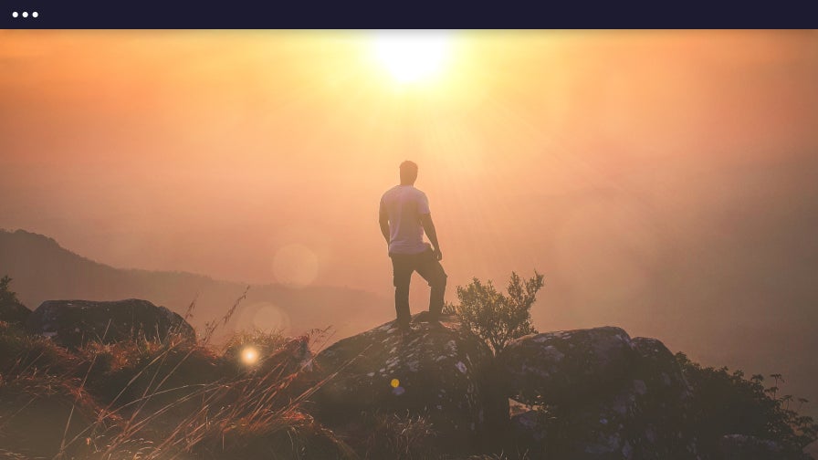 Person standing on a rocky cliff at sunset with dramatic lens flare effect