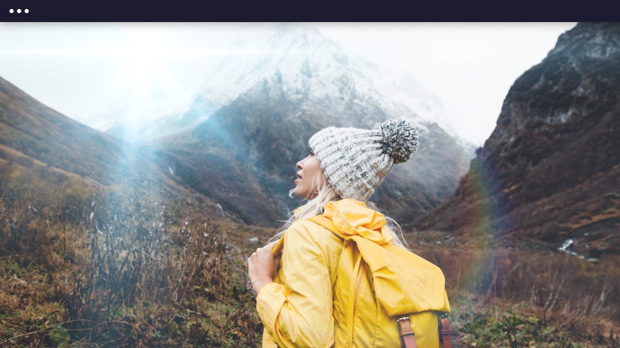 Woman in yellow jacket admiring mountains with cool-toned lens flare in the sky