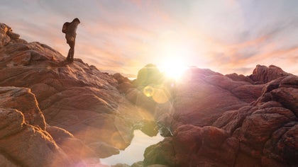 Hiker walking over rocky terrain enhanced with a warm lens flare at sunset