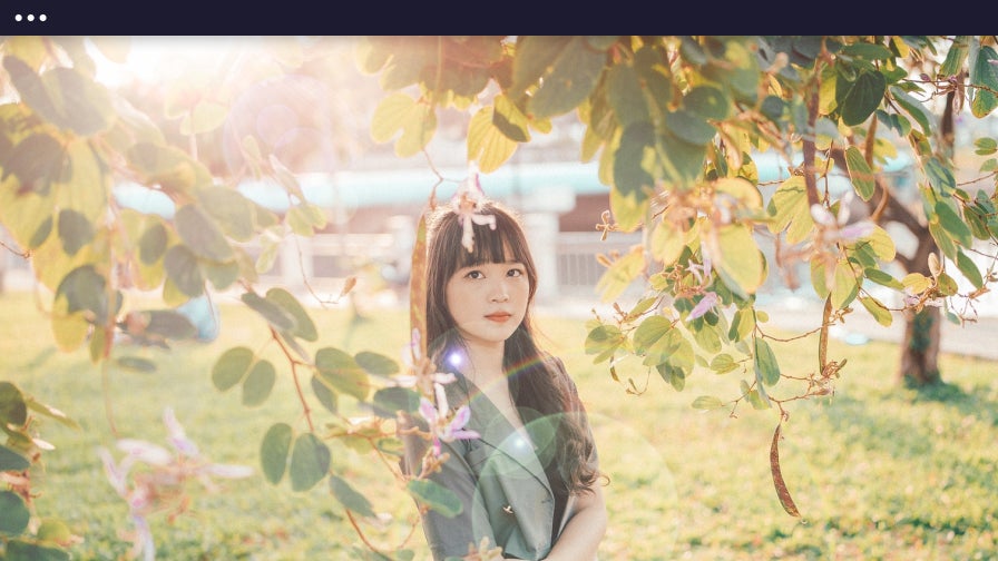 Young girl standing under a flowering tree with soft lens flare filtering through leaves